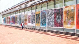 a person walks outdoors next to a row of artworks on display