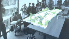 Group sitting around a large table with an illuminated, augmented reality image of buildings hovering above table.